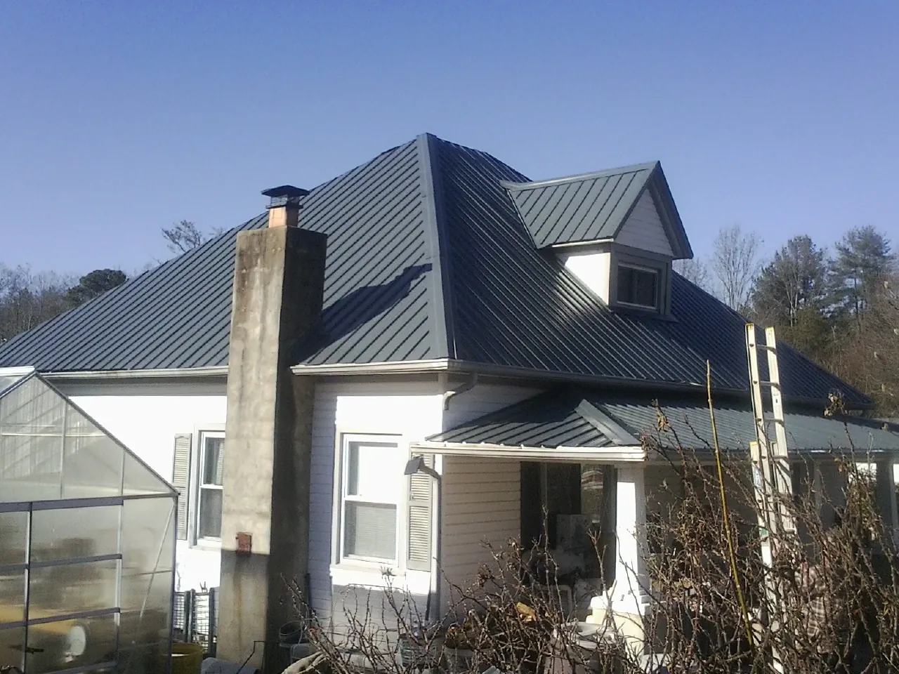 Dark blue standing seam metal roof on a white farmhouse with dormer — Slate & Tile Roof Repair by Roofing Brothers in Thatcher