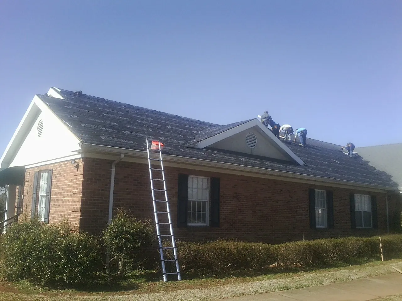 Crew tearing shingles off a brick ranch roof with a ladder set — Metal Roof Repair work by our crew in Thatcher
