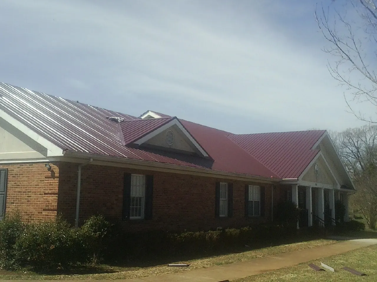 Red metal roof with gabled entries on a long brick building, from a Hail Damage Roof Repair job in Thatcher