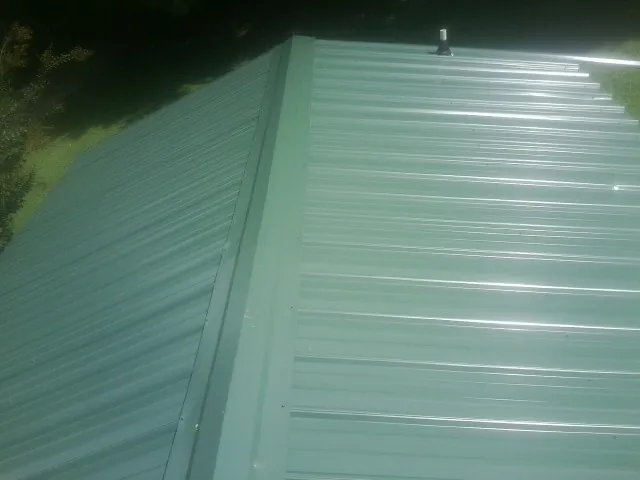 New green metal panels meeting at the ridge of a roof — Flat Roof Repair work by our crew in Thatcher