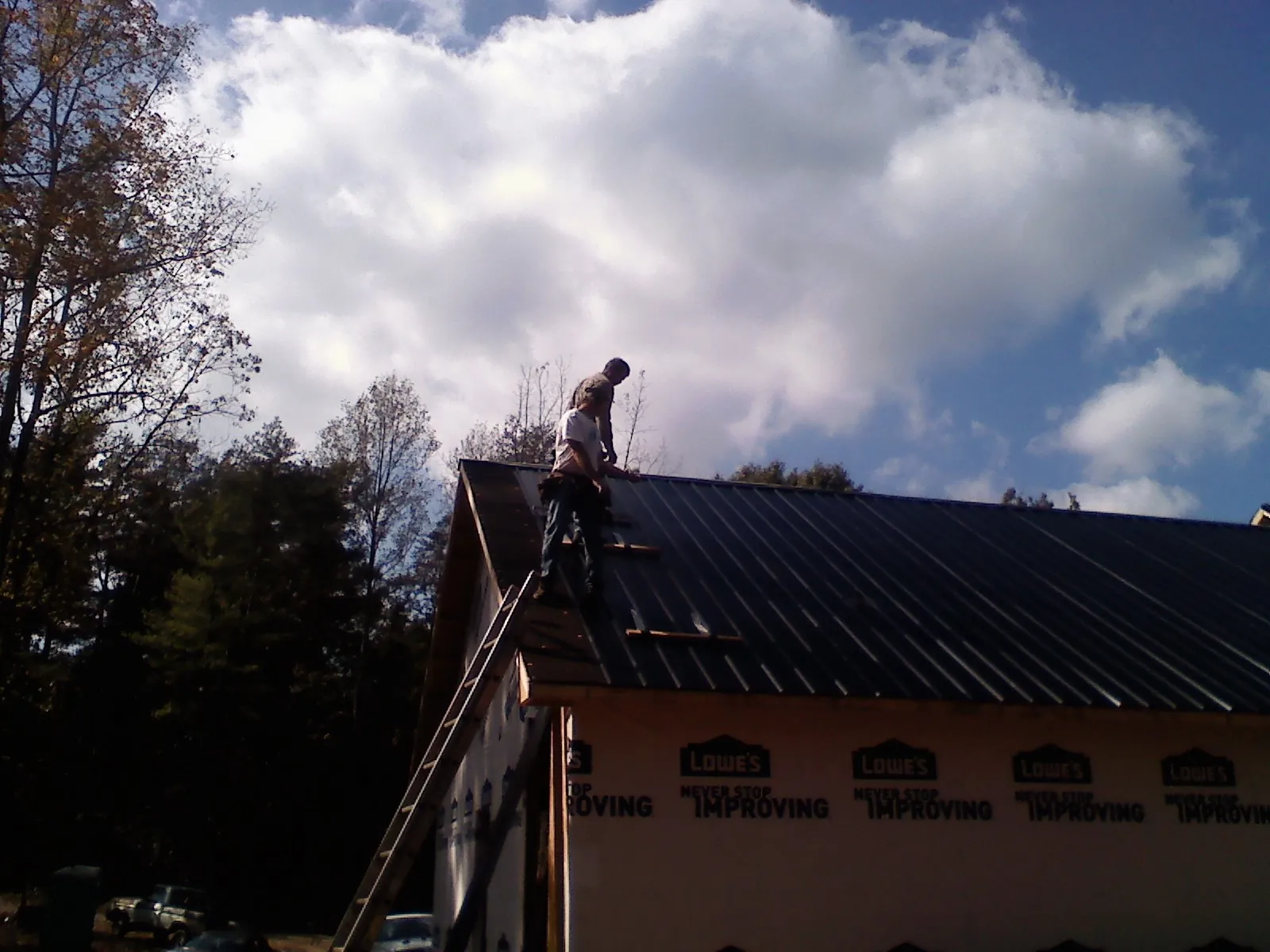 Roofer fastening dark metal panels high against a cloudy sky, from a Roof Inspection job in Thatcher