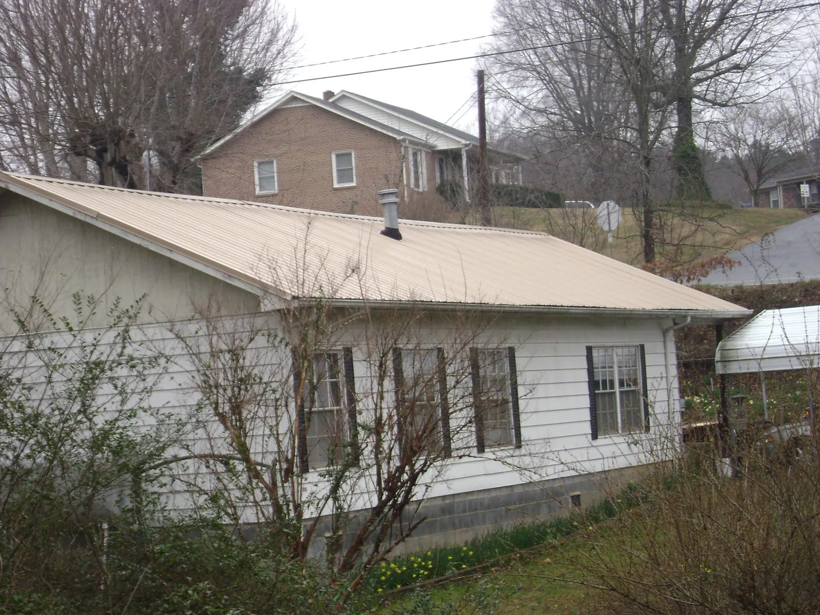 Tan metal roof on a white sided house set into a hillside — Commercial Roofing by Roofing Brothers in Thatcher
